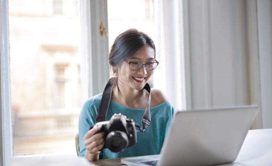 woman smiling in front of a laptop and holding a camera